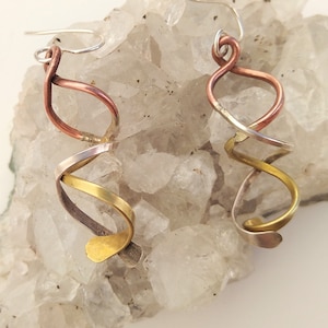 May include: A pair of dangle earrings made of twisted copper, brass, and silver wire. The earrings are a unique and modern design.