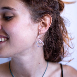 Puede incluir: Una mujer con cabello castaño rizado que lleva un pendiente de plata de forma abstracta y un collar turquesa.