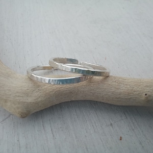 Puede incluir: Dos anillos de plata con textura martillada, apilados uno encima del otro. Los anillos están sobre una superficie de madera marrón claro.