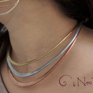 May include: A layered necklace set featuring three individual necklaces in gold, silver, and copper tones. The necklaces are worn around the neck. The image also shows a matching earring. The Neo Tribal logo is visible.