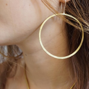 May include: A pair of large, gold hoop earrings. The earrings are made of thick, round wire and have a smooth, polished finish.