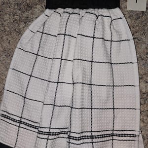 May include: White kitchen towel with a black grid pattern and a black top. The towel has a waffle weave texture and a black border. The number "1" is visible in the upper right corner.