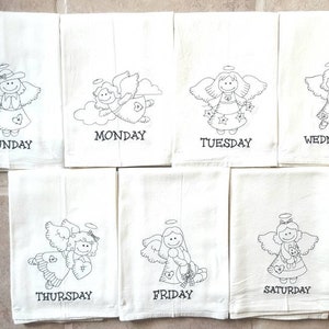 Pode incluir: Conjunto de sete panos de cozinha brancos, cada um bordado com um desenho de anjo diferente e o dia da semana em escrita preta. Os anjos t&ecirc;m asas, aur&eacute;olas e seguram v&aacute;rios objetos.