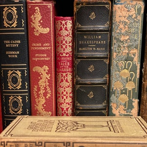 May include: A collection of vintage hardcover books with gold lettering and decorative designs on the spines. The books include titles like "The Caine Mutiny", "Crime and Punishment", "Tales of the Alhambra", "William Shakespeare", and "Great Epochs in American History".