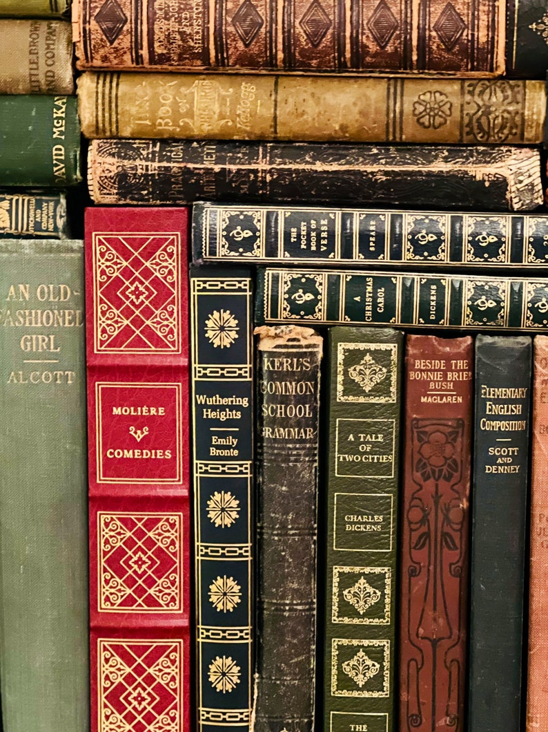 May include: A collection of antique books with various colors and designs. Titles include "Moliere Comedies", "Wuthering Heights", "A Tale of Two Cities", and "Christmas Carol". The books are stacked together, showcasing their aged covers and gold lettering.