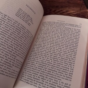 May include: An open book with the title "PRUDENCE" at the top. The pages are filled with printed text, with a focus on the text and the book's content. The book is on a dark wooden surface.