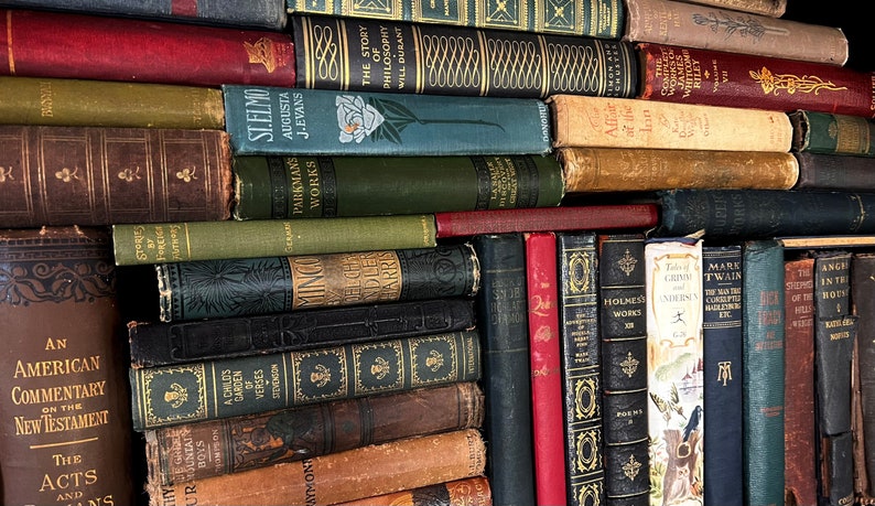 May include: A collection of antique books with various colors and titles. The spines are visible, showcasing titles like "St. Elmo" and "Mark Twain." The books are stacked, creating a vintage library aesthetic.