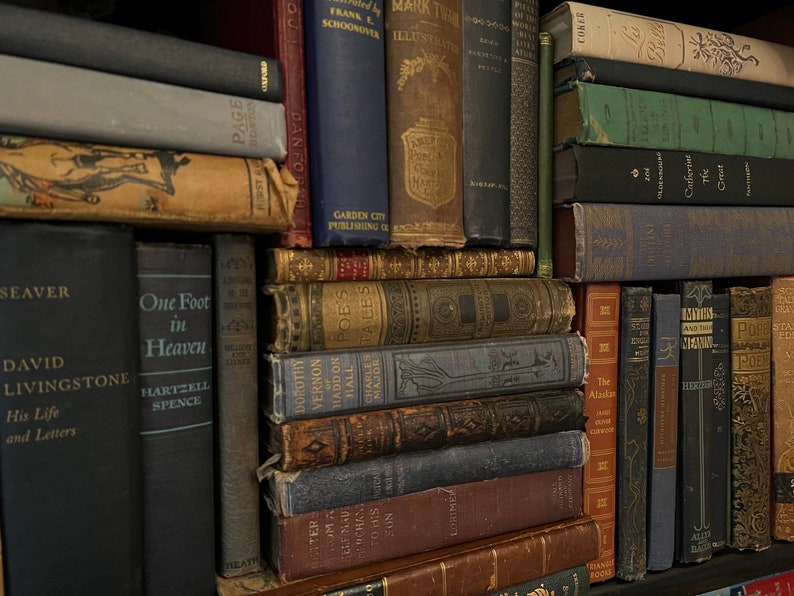 May include: A bookshelf filled with a variety of old, leather-bound books. The books are arranged in rows and columns, and many of them have titles and author names visible. The books are mostly brown, black, and red in color.