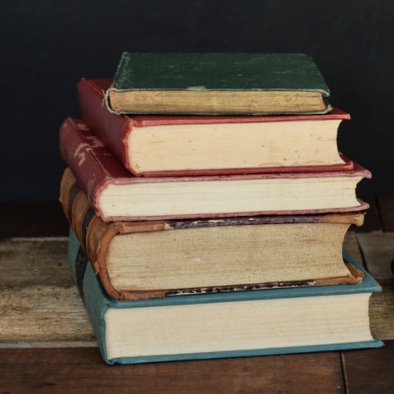 May include: A stack of five vintage hardcover books with different colored covers. The top book is green, the next is red, the next is brown, the next is red, and the bottom book is blue.