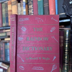 Puede incluir: Un libro de tapa dura rojo titulado "The Rainbow Dictionary" de Wendell W. Wright. La portada del libro presenta ilustraciones de varios objetos, incluyendo un martillo, un paraguas, un tren y un paracaídas.