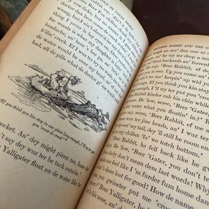 May include: Open book with aged, yellowed pages. Text and an illustration are visible. The book is open to a page with a drawing of a person in a boat. The text is in black ink.