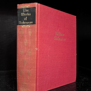 May include: A red hardcover book with the title "The Works of Shakespeare" on the spine. The book is on a black surface.
