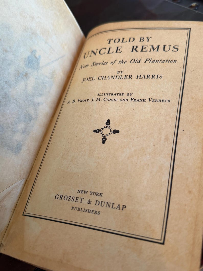 May include: An open book with a tan cover featuring the title "Told by Uncle Remus" and the author's name, Joel Chandler Harris. The book is illustrated by A.B. Frost, J.M. Conde, and Frank Verbeck. Published by Grosset & Dunlap, New York.