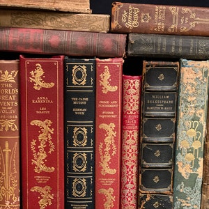May include: A close-up view of a bookshelf filled with vintage hardcover books. The books have various colors, including red, brown, and black. The titles of the books are visible, including "The World's Great Events", "Anna Karenina", "The Caine Mutiny", "Crime and Punishment", "William Shakespeare", and "Stories of Courage and Heroism".