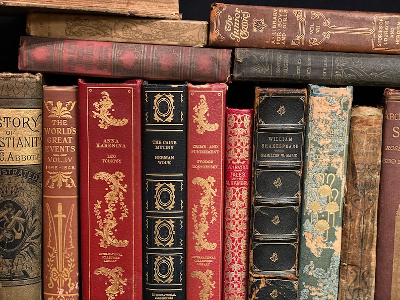 May include: A close-up view of a bookshelf filled with vintage hardcover books. The books have various colors, including red, brown, and black. The titles of the books are visible, including "The World's Great Events", "Anna Karenina", "The Caine Mutiny", "Crime and Punishment", "William Shakespeare", and "Stories of Courage and Heroism".