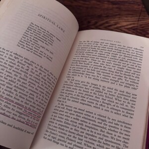 May include: An open book with text on aged paper, featuring the title "SPIRITUAL LAWS" at the top of the page. The pages are yellowed, suggesting age, and the text is in a classic serif font. The book is on a dark wooden surface.