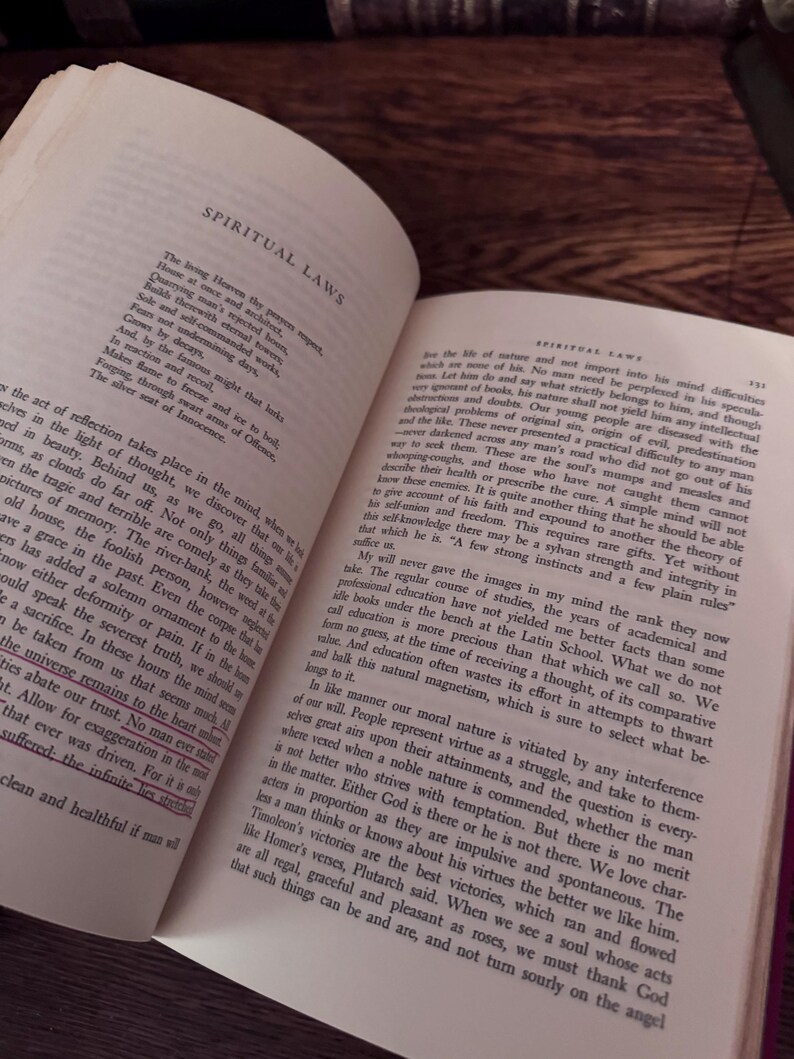May include: An open book with text on aged paper, featuring the title "SPIRITUAL LAWS" at the top of the page. The pages are yellowed, suggesting age, and the text is in a classic serif font. The book is on a dark wooden surface.