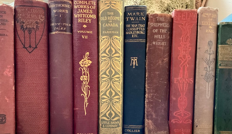 May include: A collection of antique books with various titles and colors. The spines display titles like "Hawthorne's Works," "Mark Twain," and "The Old Regime in Canada." The books have decorative gold and embossed lettering.