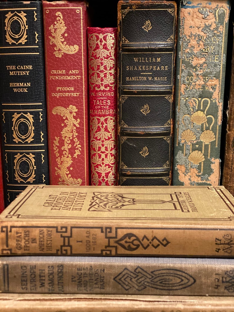 May include: A collection of vintage hardcover books with gold lettering and decorative designs on the spines. The books include titles like "The Caine Mutiny", "Crime and Punishment", "Tales of the Alhambra", "William Shakespeare", and "Great Epochs in American History".