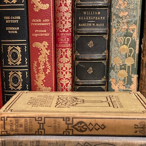 May include: A collection of vintage hardcover books with gold lettering and decorative designs on the spines. The books include titles like "The Caine Mutiny", "Crime and Punishment", "Tales of the Alhambra", "William Shakespeare", and "Great Epochs in American History".