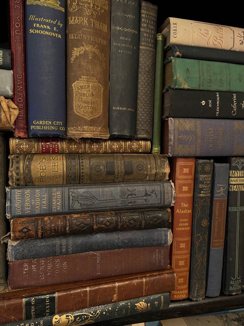 May include: A bookshelf filled with vintage hardcover books. The books are arranged in a vertical stack, with the spines facing outward. The books are mostly brown, blue, and green, with gold lettering. Some of the titles include "Mark Twain Illustrated", "Master Pieces of the World's Best Literature", "The Alaskan", and "St. George for England".