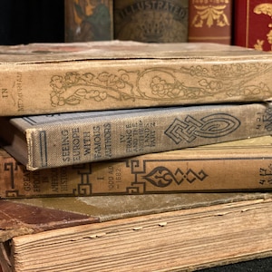 May include: A stack of vintage hardcover books with brown, blue, and gold covers. The top book has the title "In Memoriam" and the bottom book has the title "Great Epochs in American History."