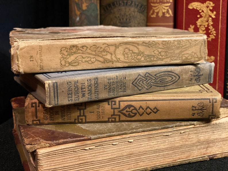 May include: A stack of vintage hardcover books with brown, blue, and gold covers. The top book has the title "In Memoriam" and the bottom book has the title "Great Epochs in American History."