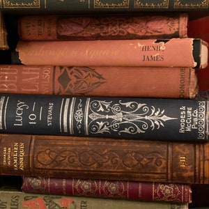 May include: A stack of vintage hardcover books with ornate designs and titles like "New Arabian Nights", "The Air of Russia", "The Square", "Lucky 10", and "Daddy Long-Legs".