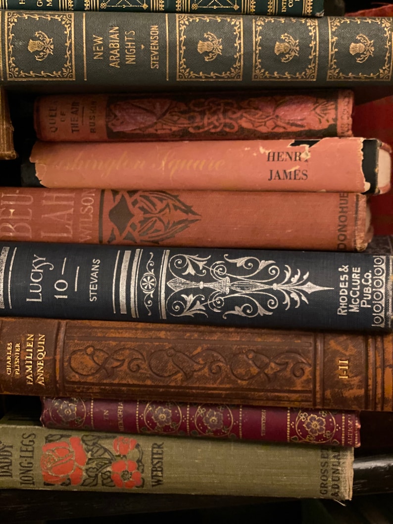 May include: A stack of vintage hardcover books with ornate designs and titles like "New Arabian Nights", "The Air of Russia", "The Square", "Lucky 10", and "Daddy Long-Legs".