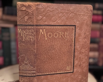 Könnte beinhalten: Ein braunes, ledergebundenes Buch mit goldenen Lettern auf dem Rücken, die "Moores Poems" und "Moore" auf dem vorderen Umschlag lesen. Der Umschlag ist mit einem Kiefernbaumdesign geprägt.