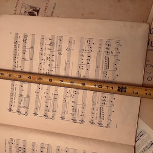 May include: A close-up of a sheet of music with musical notes printed on it. A measuring tape is placed across the sheet of music, with the numbers 1 through 16 visible. The text "Don't C" and "Our Ha Jesus" is visible on the page.