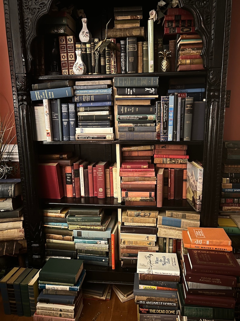May include: A black wooden bookshelf filled with books. The shelves are stacked high with books of various sizes and colors. There are also a few decorative items on the shelves, including a pineapple, a vase, and a plant.