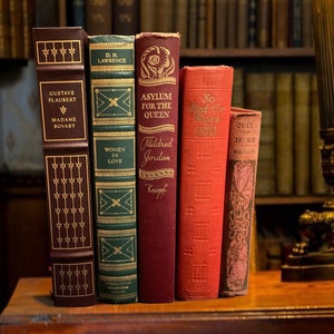 May include: Five vintage hardcover books with gold lettering on the spines. The books are arranged vertically from left to right. The titles are "Madame Bovary", "Women in Love", "Asylum for the Queen", "So Red the Rose", and "Queen of the Air".