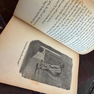May include: An open book with aged, yellowed pages. The text is in black ink, with an illustration of a person lying down. The illustration is in black and white. The text reads "So he holler down thoo de crack."