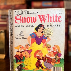 May include: A vintage copy of "Walt Disney's Snow White and the Seven Dwarfs," a Little Golden Book. The cover features an illustration of Snow White and the seven dwarfs. The book has a gold seal that reads "a Billion Golden Memories."