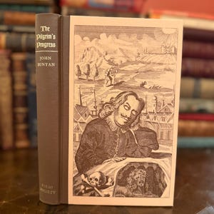 May include: A hardcover book titled "The Pilgrim's Progress" by John Bunyan. The book has a brown cover with gold lettering. The book's illustration depicts a man, a landscape, and a skull.