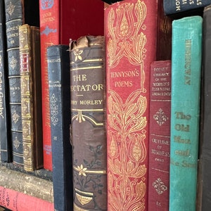 May include: A bookshelf filled with vintage hardcover books with various titles and authors. The books are arranged in a vertical row and have different colors and designs. Some of the titles include "The Spectator", "Tennyson's Poems", "Pocket Library of the World's Essential Knowledge", and "The Old Man and the Sea".