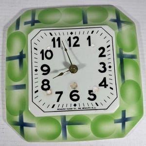 May include: A square wall clock with a white face, black Arabic numerals, and thin black hands. The border features a light green pattern of circles and dark blue crosses. The text Newark Clock Co. Inc. Newark N.J. is printed at the bottom.