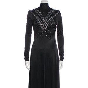 May include: A long black dress with a high neckline and long sleeves. The dress is embellished with a pattern of small, sparkling rhinestones across the shoulders and chest. The dress has a flowing skirt.