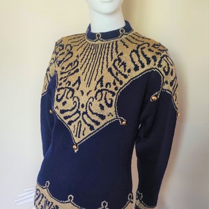 May include: A navy blue sweater with a gold patterned design and gold buttons. The sweater has a high neck and long sleeves.