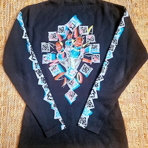 May include: Black long-sleeved shirt with a colorful geometric design featuring a central image of a group of people with their hands raised.