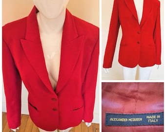 May include: A vibrant red blazer with a classic two-button closure and notched lapels. The tailored jacket features two front pockets and is displayed on a mannequin. The label reads "ALEXANDER MCQUEEN MADE IN ITALY".