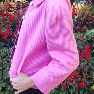 May include: A pink ribbed jacket with white buttons and a long sleeve. The jacket is made of a soft, stretchy material and has a relaxed fit.