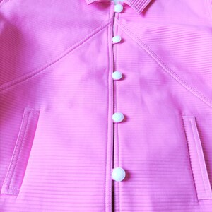 May include: A pink jacket with a ribbed texture and a row of white buttons down the front.
