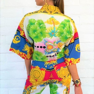 May include: A white, blue, red and yellow patterned shirt and trousers set. The shirt has a short sleeve and a collar. The trousers are a straight leg style.