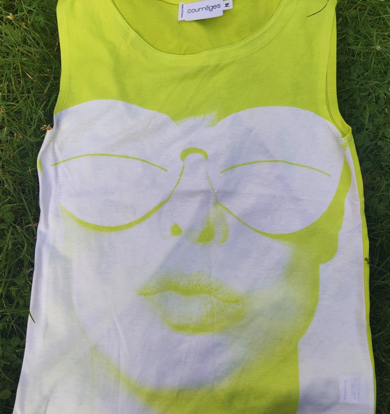 May include: A lime green sleeveless tank top with a white graphic print of a woman's face wearing sunglasses. The graphic is in a retro style with a bold outline. The text "courr&egrave;ges" is printed on the top in black.