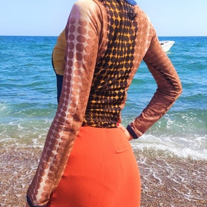 May include: A long-sleeved shirt with a brown and black polka dot pattern. The shirt is sheer and has a scoop neck. The model is wearing a red skirt.