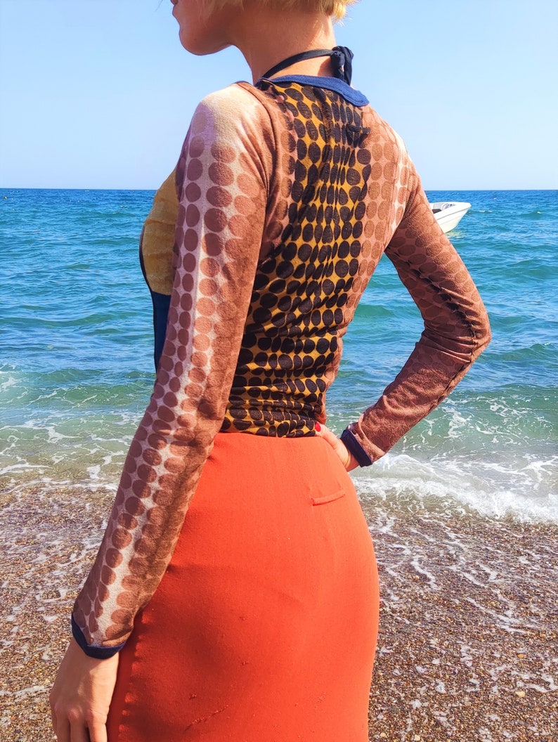May include: A long-sleeved shirt with a brown and black polka dot pattern. The shirt is sheer and has a scoop neck. The model is wearing a red skirt.