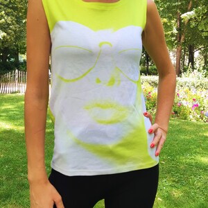 May include: A neon yellow sleeveless shirt with a white graphic of a face wearing sunglasses. The face is partially obscured by the sunglasses.