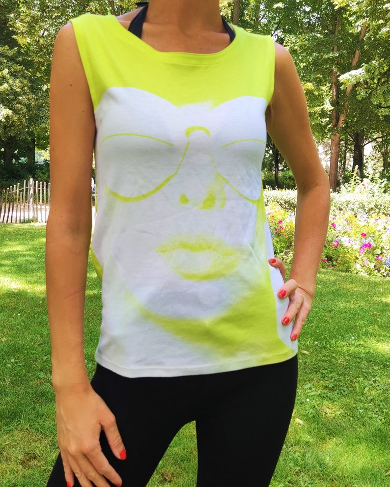 May include: A neon yellow sleeveless shirt with a white graphic of a face wearing sunglasses. The face is partially obscured by the sunglasses.